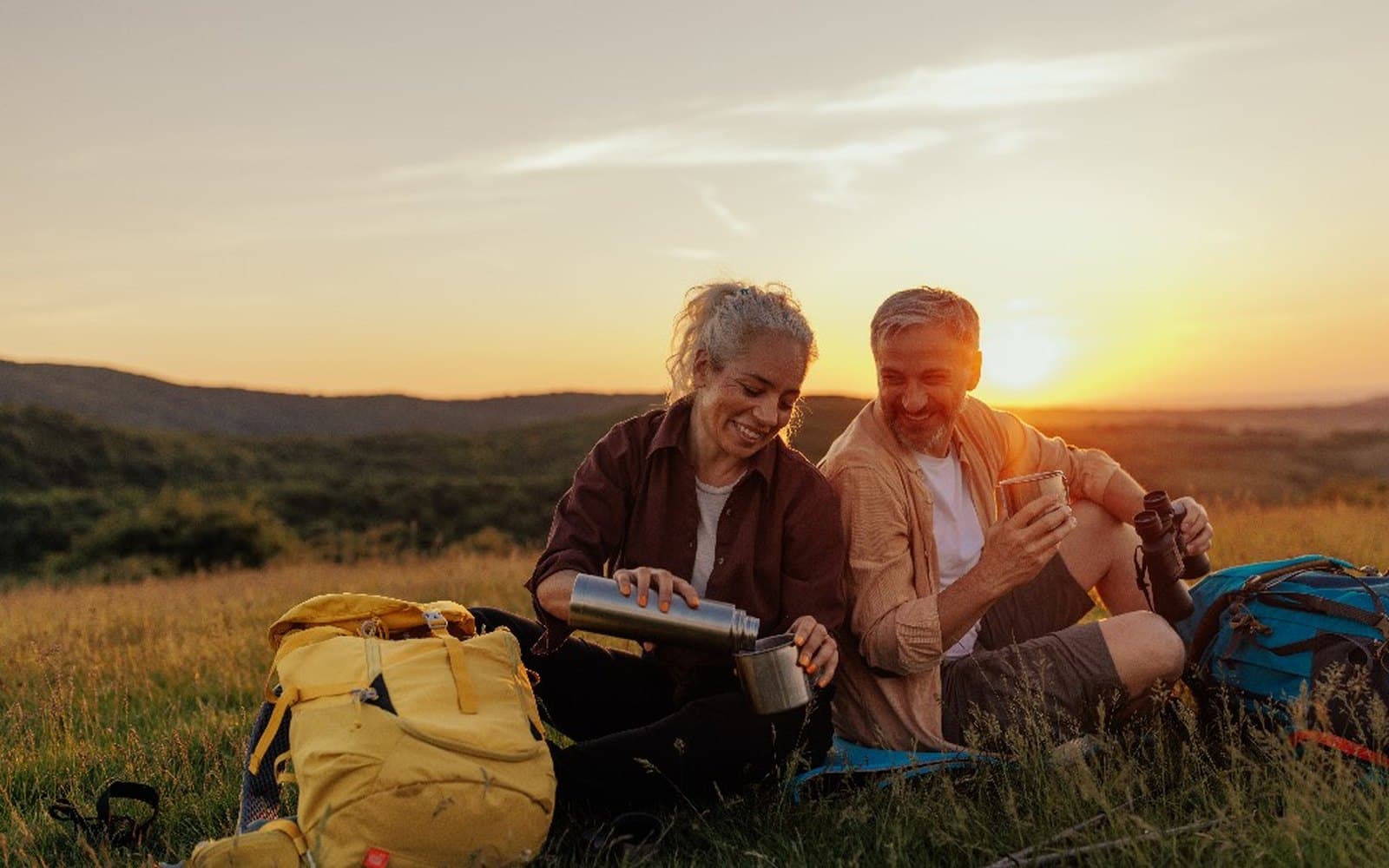 A couple resting on a hilltop at sunset.